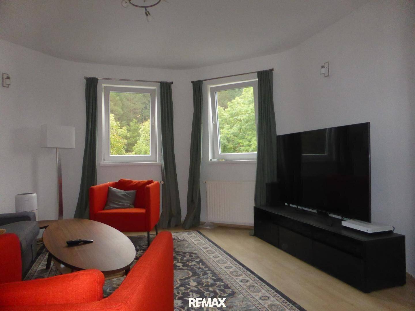 Gemütliches Wohnzimmer mit modernen Möbeln, Teppich und Blick ins Grüne.
