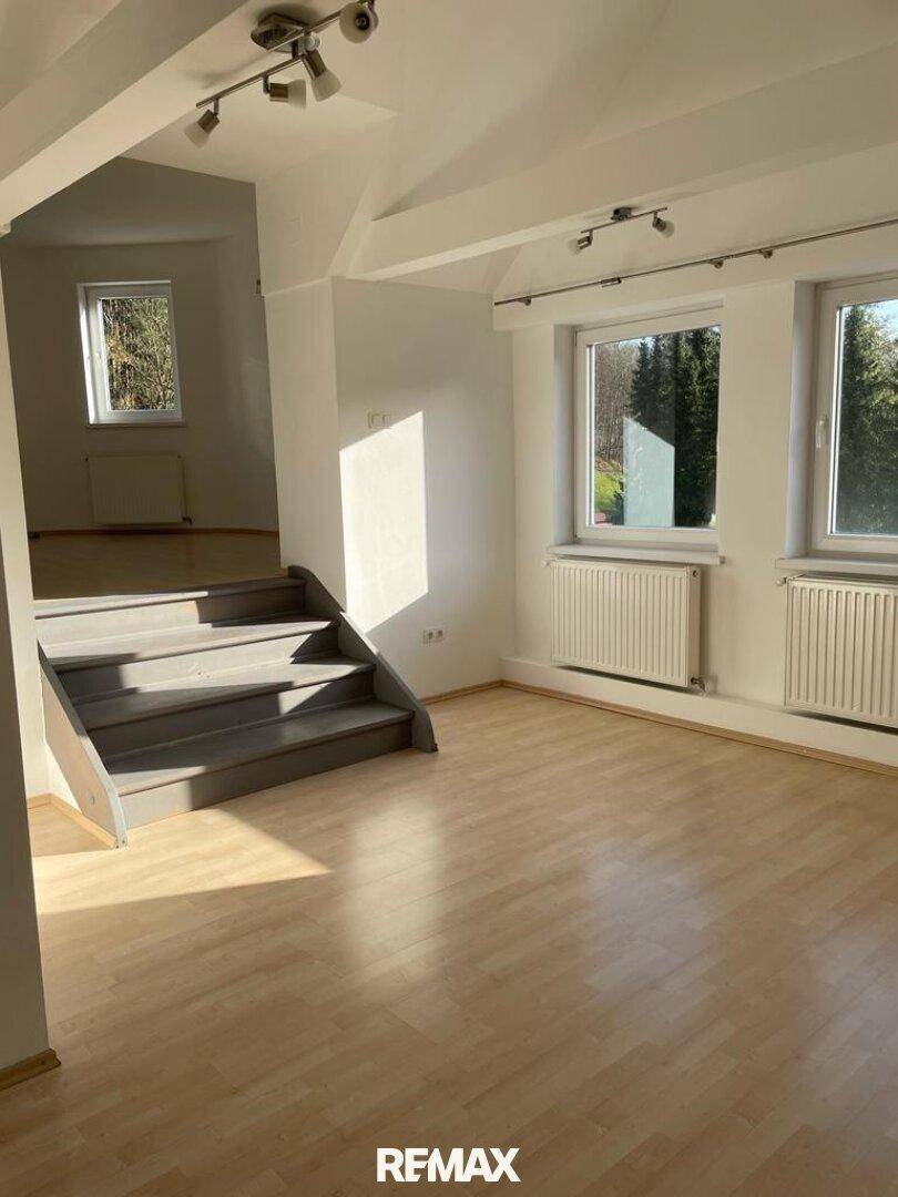 Heller Wohnbereich mit Laminatboden, weiß gestrichenen Wänden und Treppenzugang.