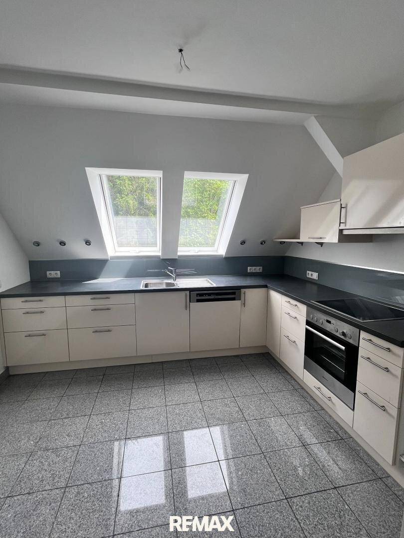 Moderne Einbauküche mit hellen Schränken, dunkler Arbeitsplatte und Dachfenstern für viel Licht.