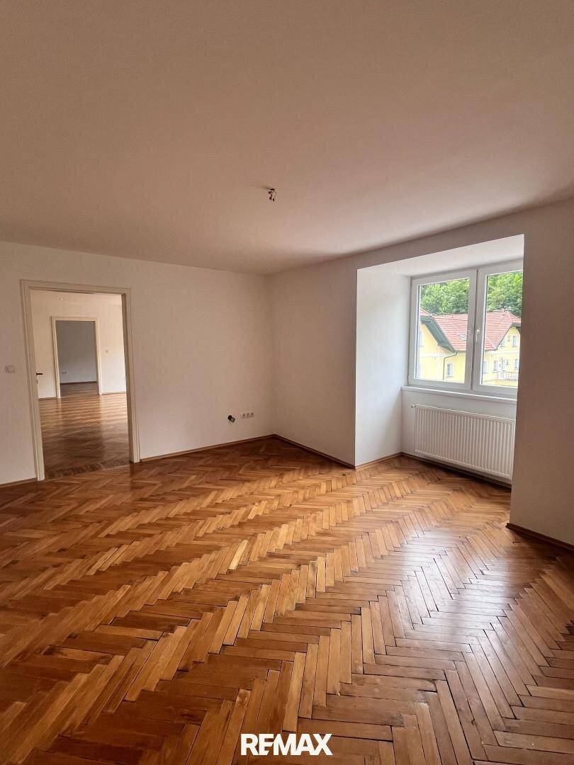 Freundlicher Raum mit Fischgrätparkett und großem Fenster, ideal als Wohn- oder Arbeitsbereich.