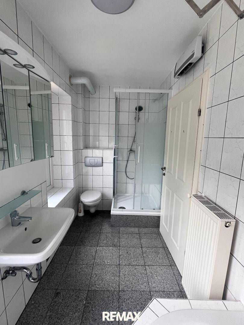 Gefliestes Badezimmer mit Dusche, WC und Waschbecken, ausgestattet mit einem Heizkörper.