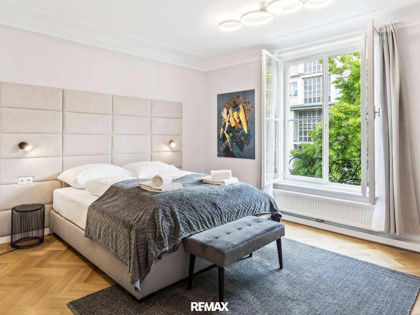 Komfortables Schlafzimmer mit gepolstertem Kopfteil, Parkettboden und Blick ins Grüne.