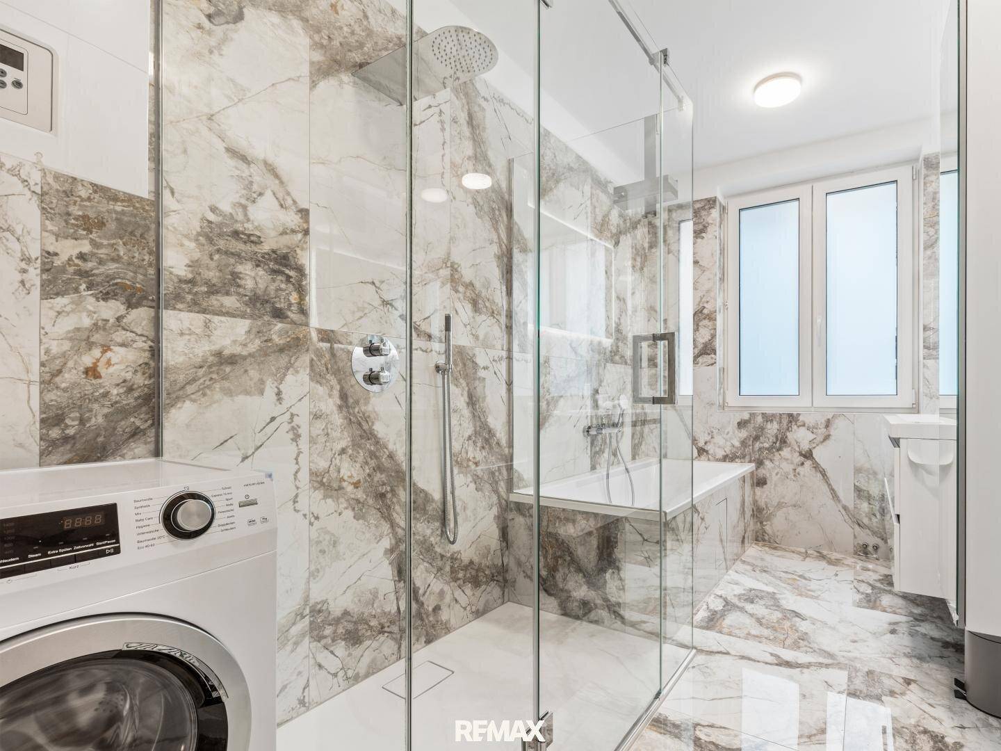 Elegantes Badezimmer mit Marmorfliesen, Glasdusche und integrierter Badewanne.