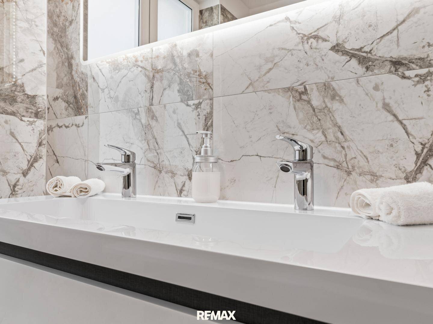 Doppelwaschbecken mit modernen Armaturen und Marmorfliesen im Badezimmer.