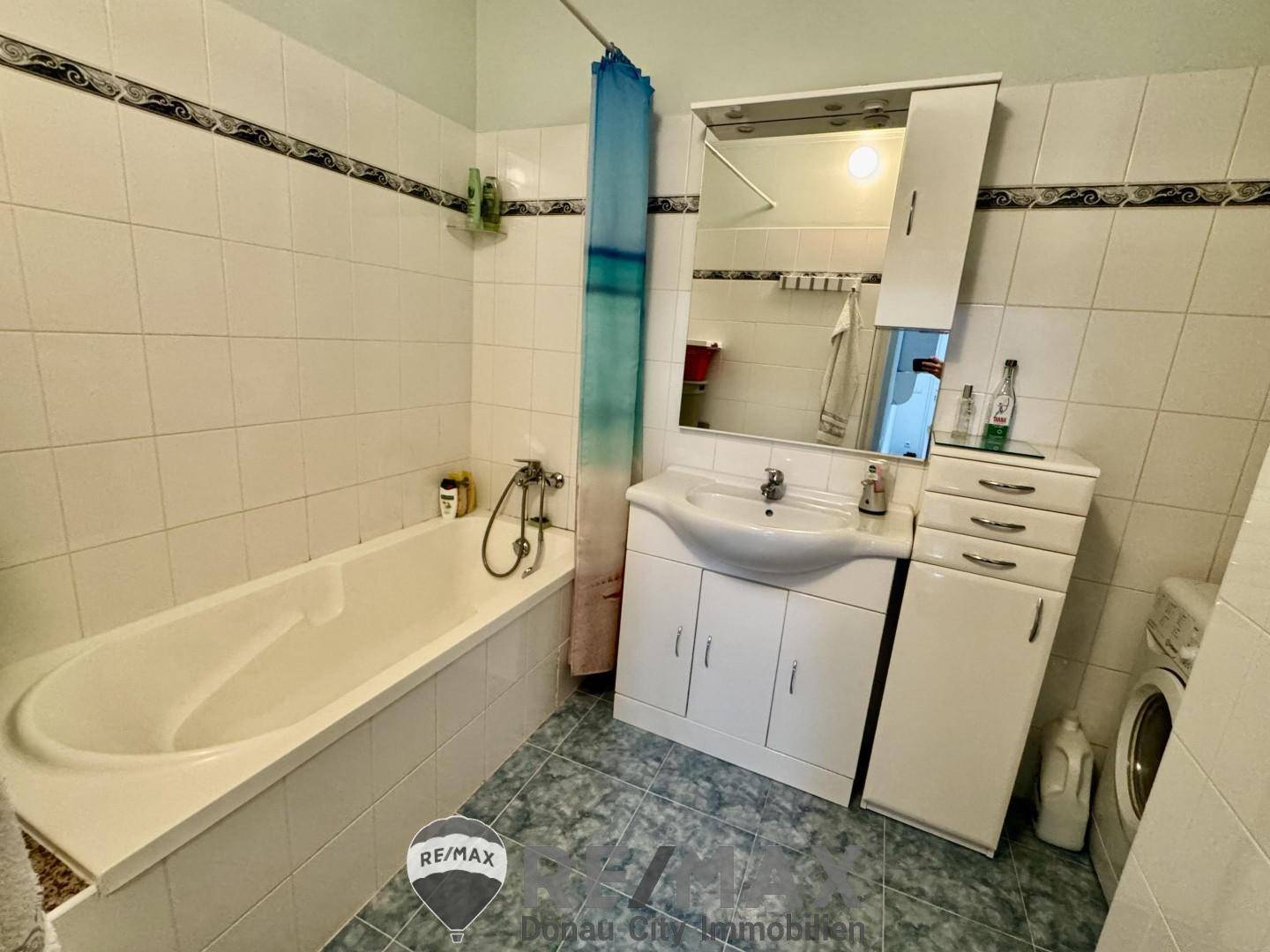 Badezimmer mit Badewanne, Waschbecken, Spiegelschrank und hellen Fliesen.