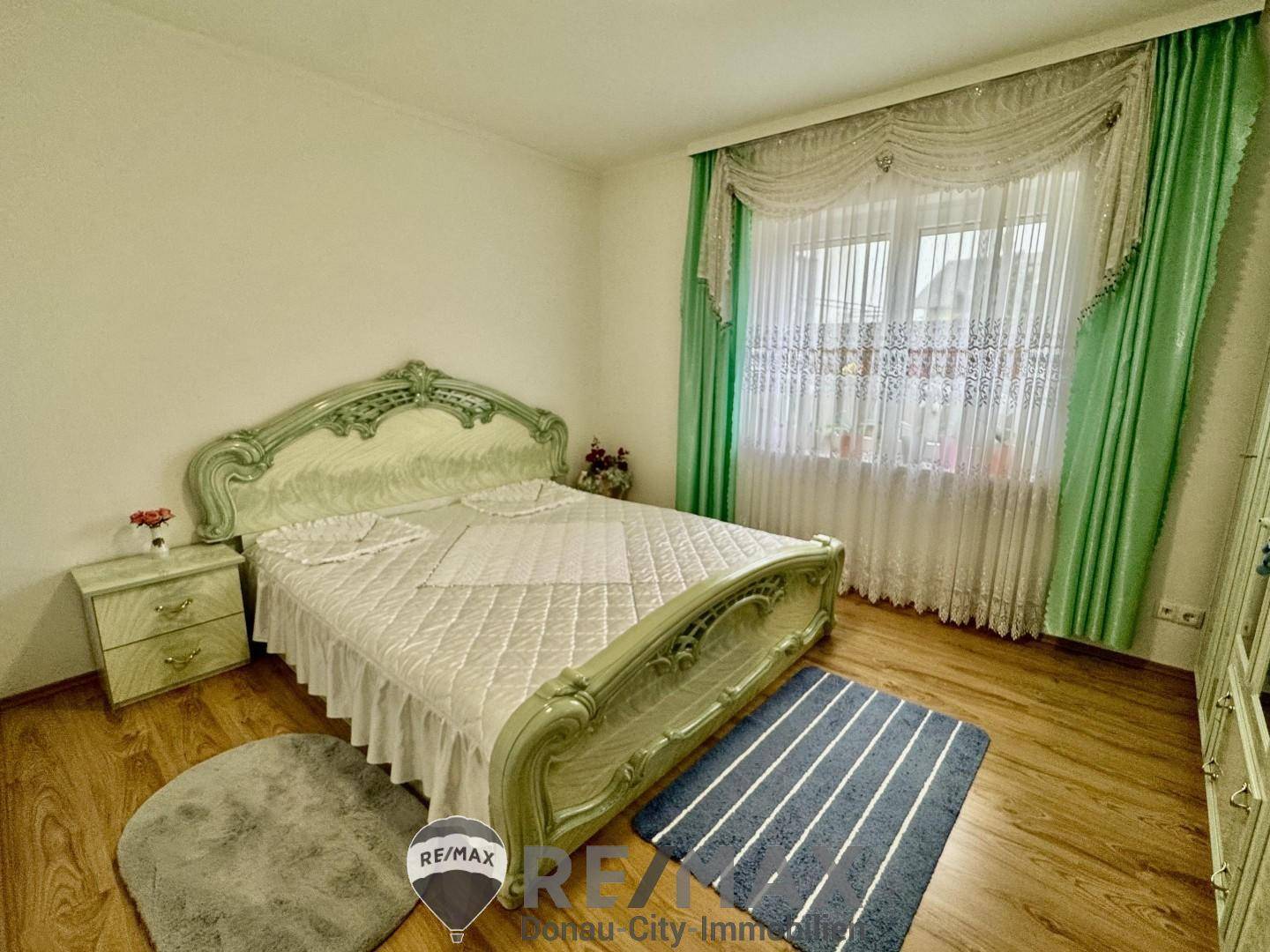 Schlafzimmer mit klassischem Bett, Laminatboden und grünen Vorhängen.