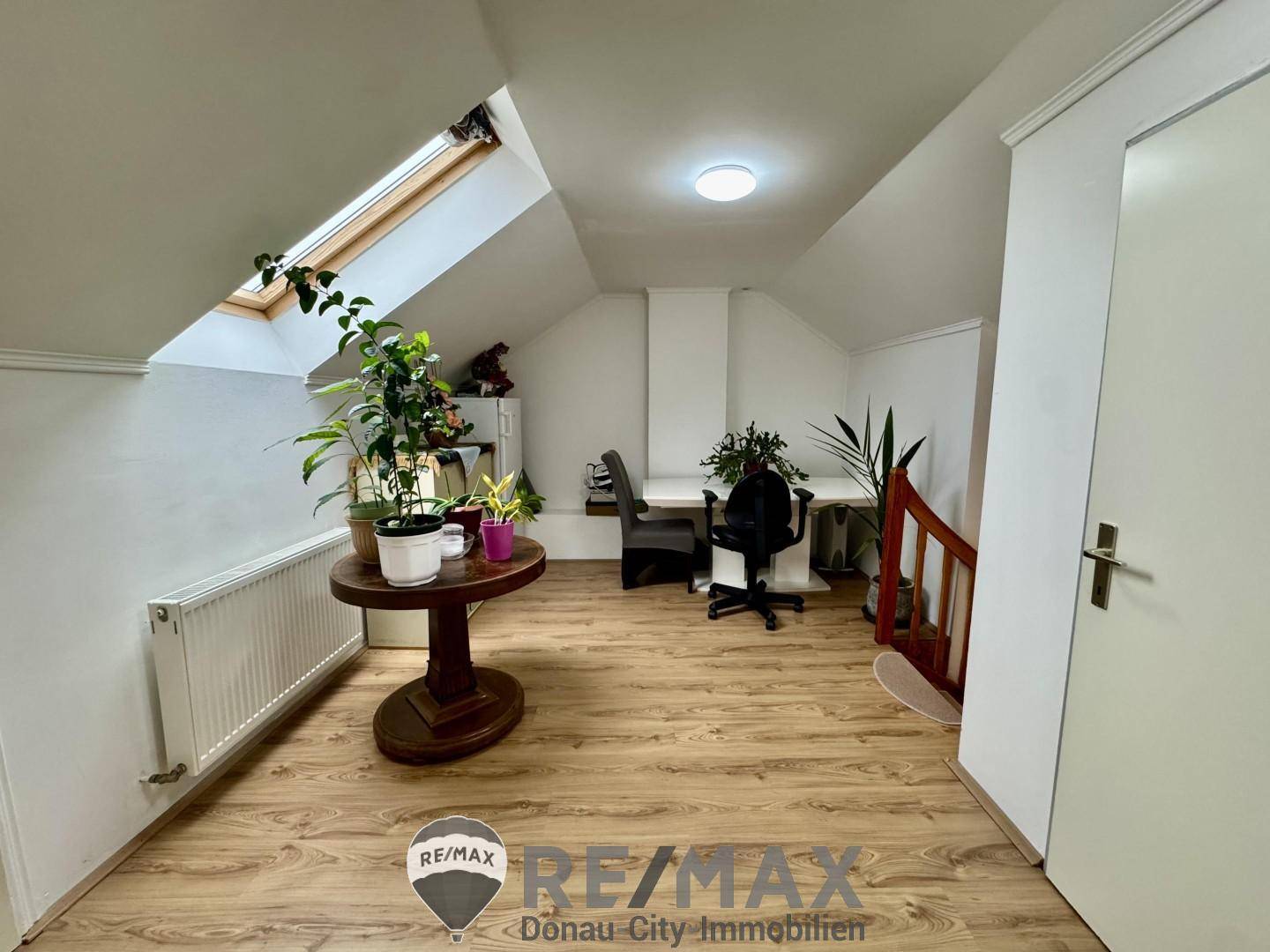 Helles Dachgeschoss-Büro mit Laminatboden, Schreibtisch und Pflanzen.