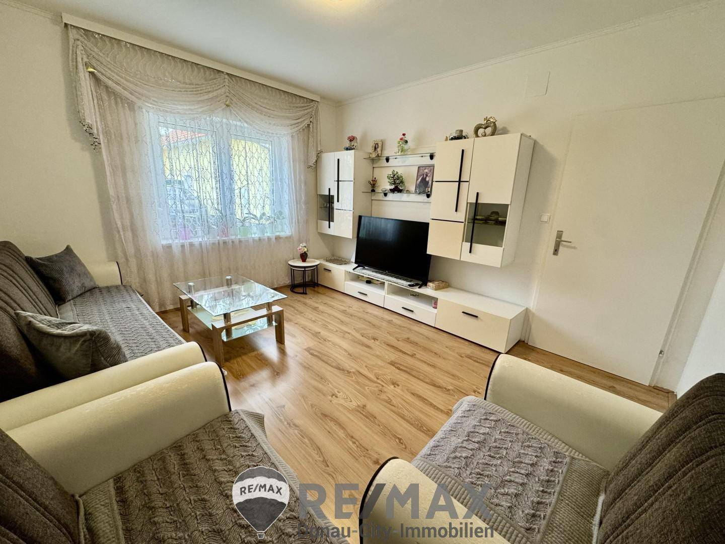 Gemütliches Wohnzimmer mit Laminatboden, großem Fenster und heller Einrichtung.