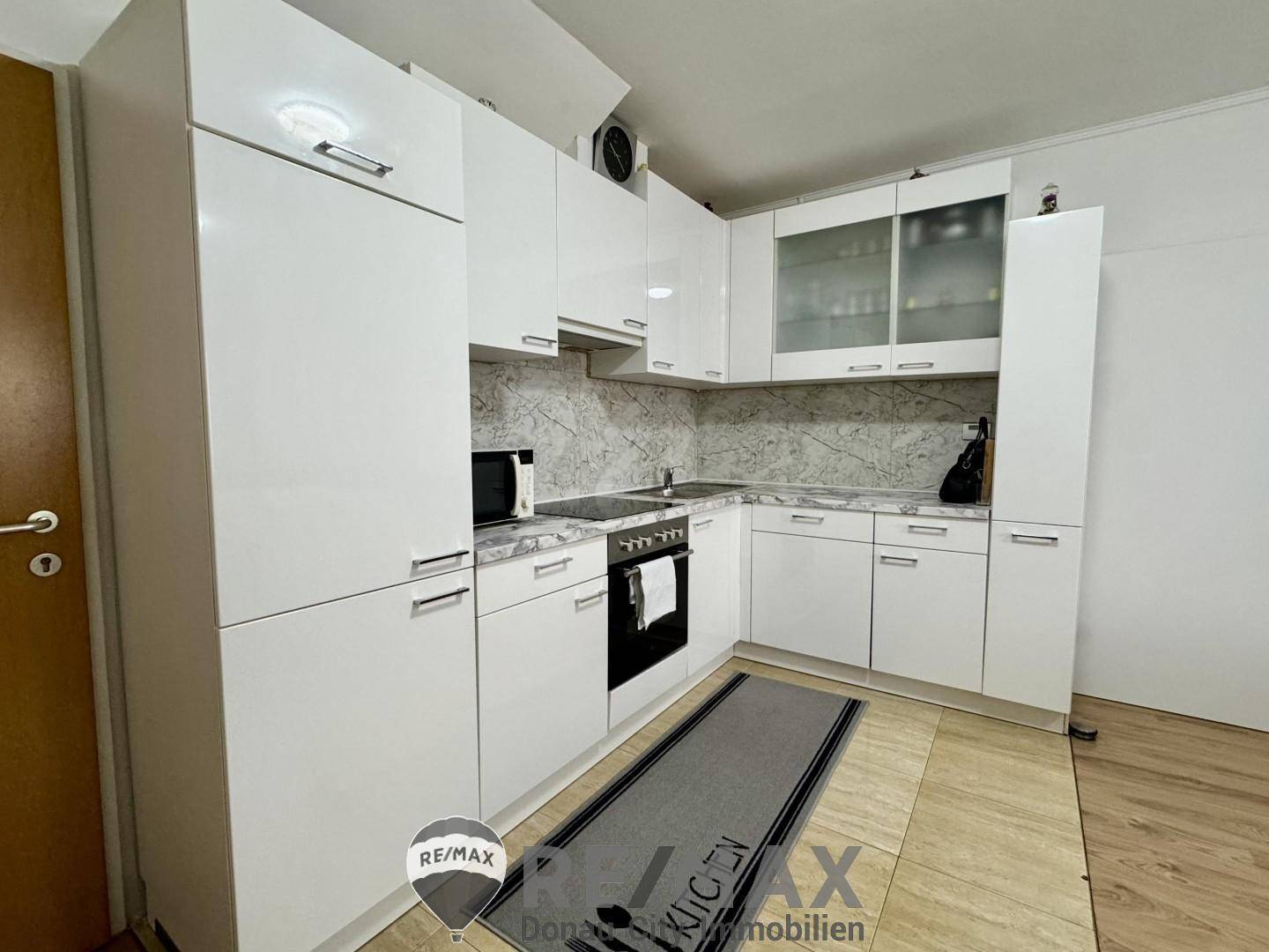 Funktionale Küche mit weißen Hochglanzschränken, integrierten Geräten und Fliesenboden.