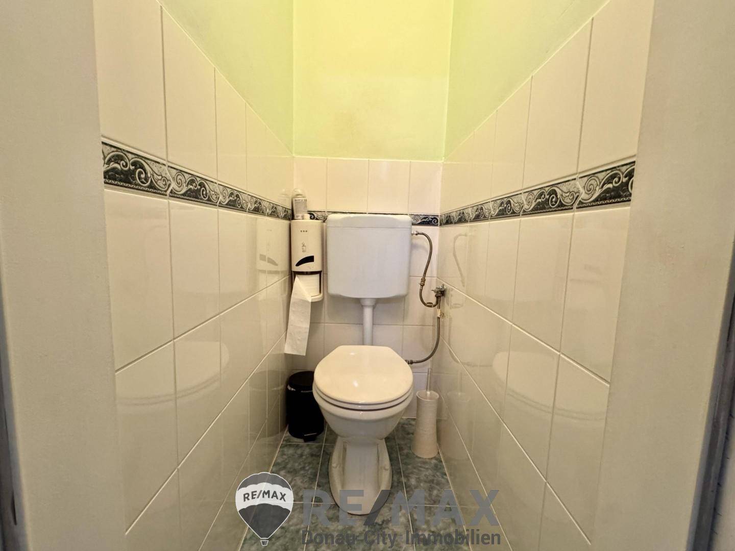 Separates WC mit Toilette und hellen Wand- und Bodenfliesen.