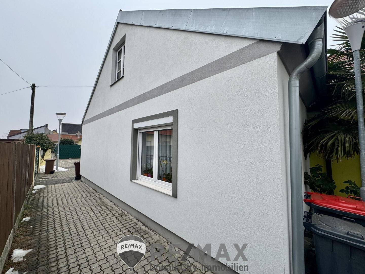 Rückseite des Hauses mit schrägem Dach und einem Fenster im Dachgeschoss.