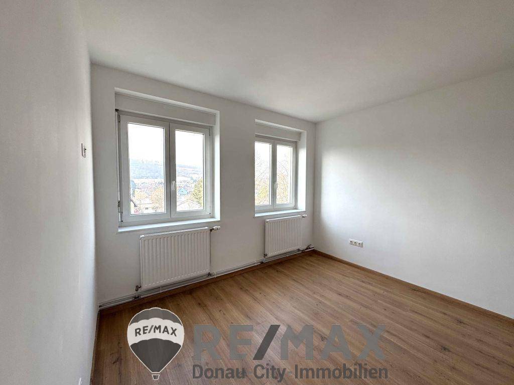 Ruhiges Schlafzimmer mit Holzfußboden und Blick ins Grüne durch die Fenster.