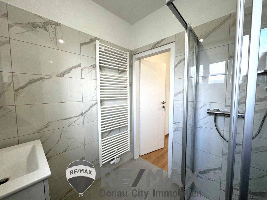 Modernes Badezimmer mit großformatigen Fliesen, Dusche und beheiztem Handtuchhalter.