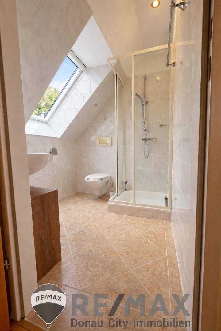 Modernes Badezimmer mit Dusche, WC und Dachfenster, hell gefliest.