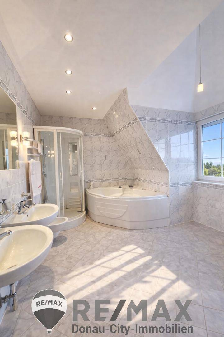 Geräumiges Badezimmer mit Doppelwaschbecken, Eckbadewanne und Duschkabine, hell gefliest.