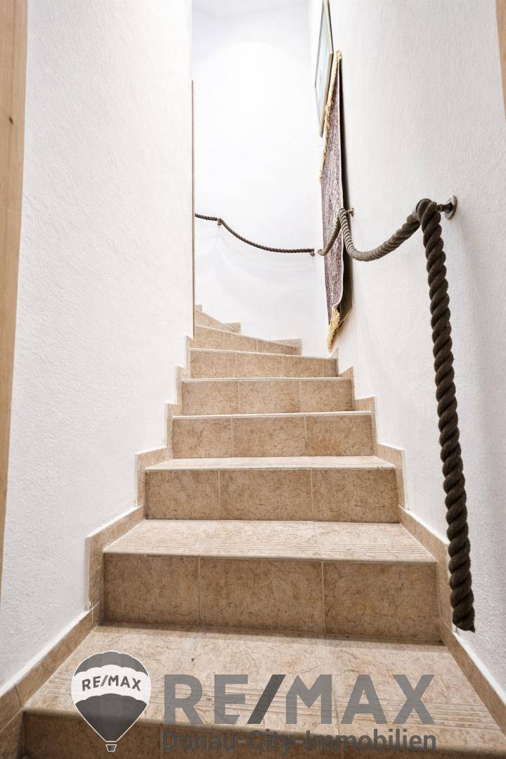 Steile Treppe mit Fliesenstufen und rustikalem Seilgeländer, führt in den oberen Bereich.