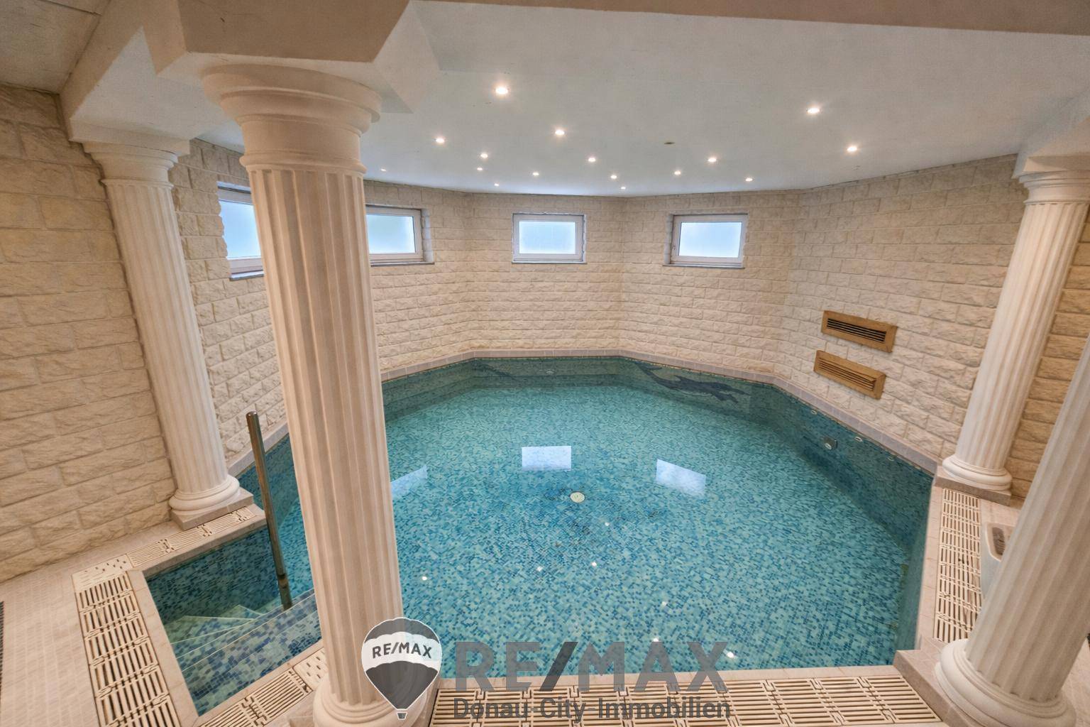 Exklusiver Innenpool mit Säulen und Mosaikfliesen, umgeben von Steinwänden.