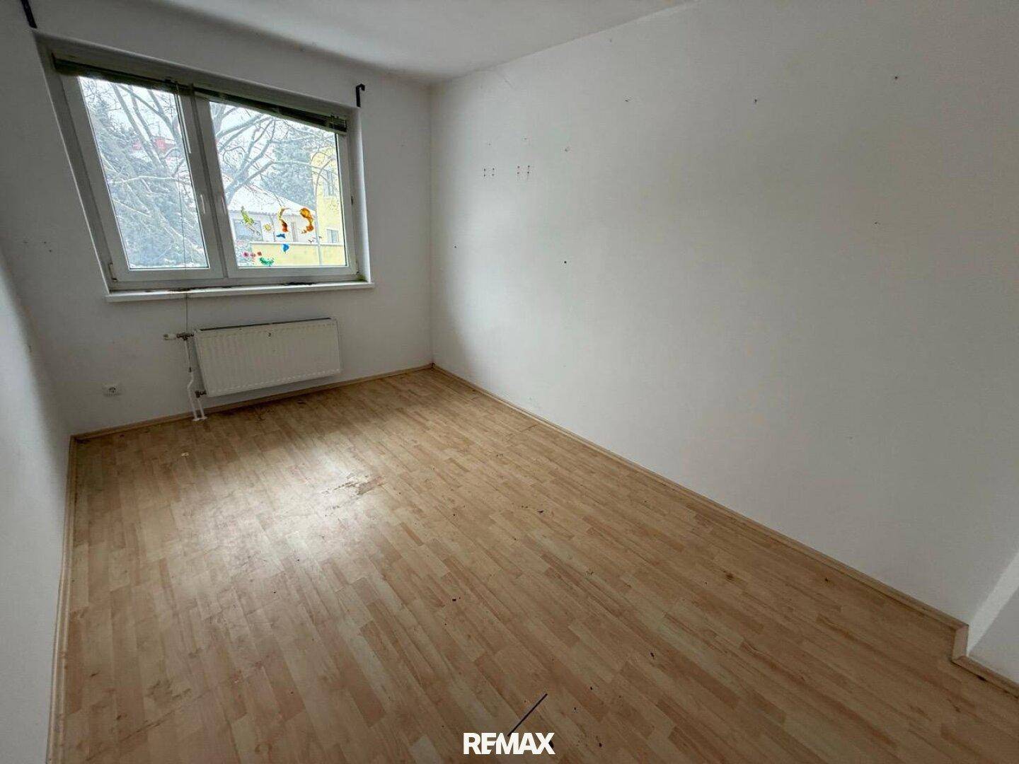 Helles Schlafzimmer mit Laminatboden, weiß gestrichenen Wänden und einem Fenster.