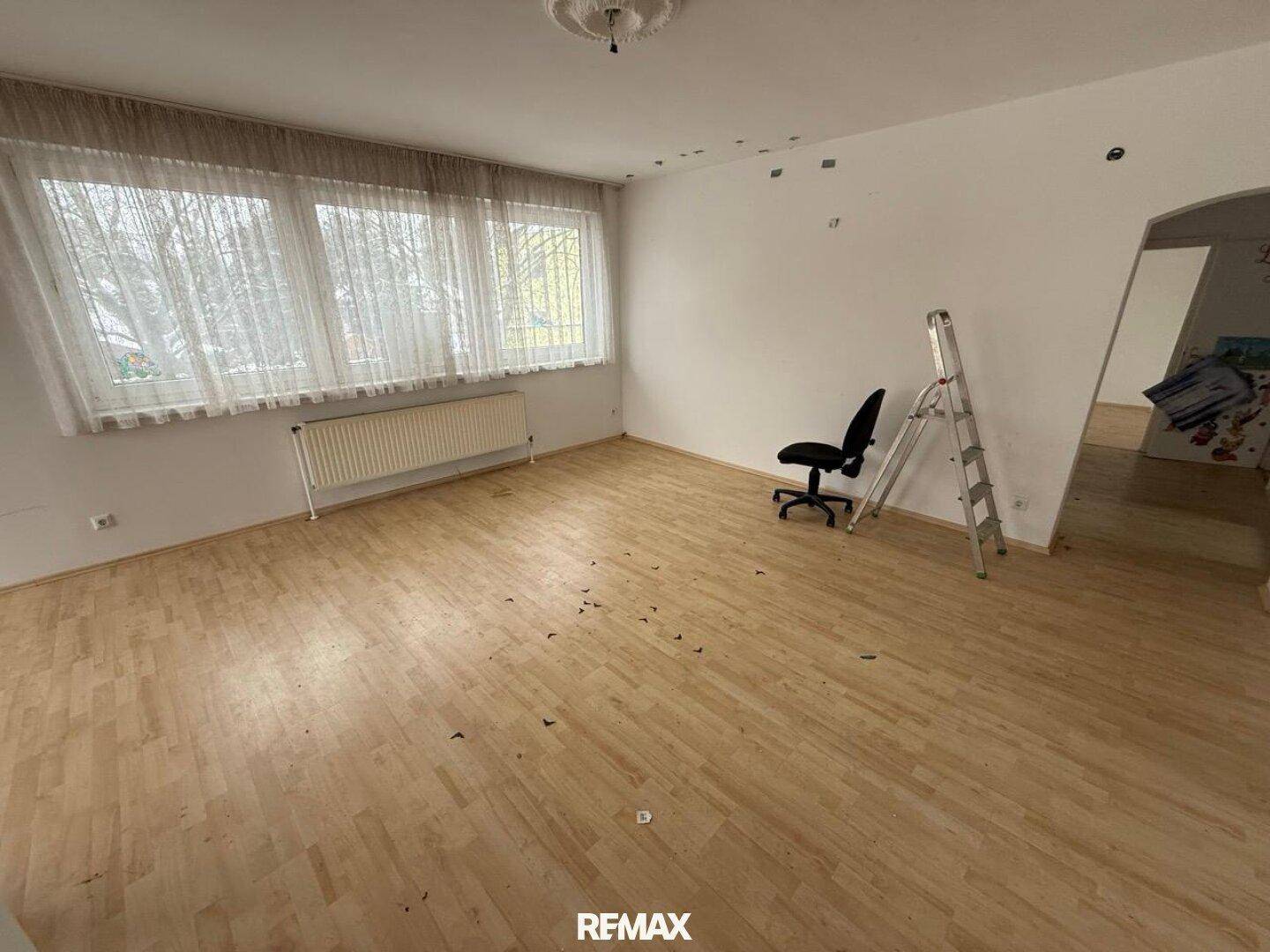 Heller Wohnbereich mit Laminatboden, großen Fenstern und einem Heizkörper.