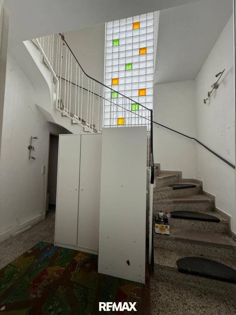 Treppenhaus mit Terrazzoboden, Geländer und einem farbigen Glasbausteinfenster.