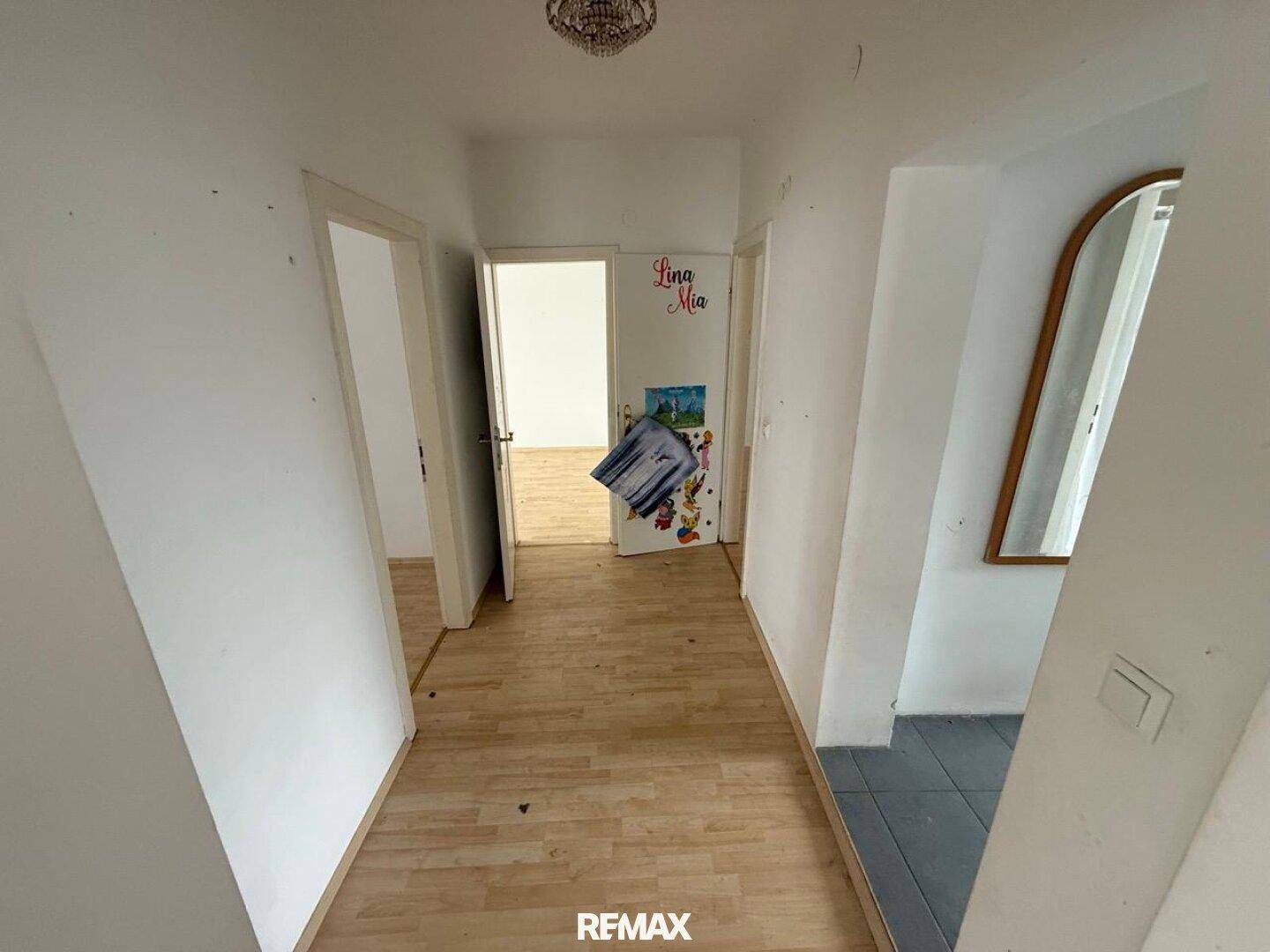Langer Flur mit hellem Laminatboden, weißen Wänden und einem Spiegel.