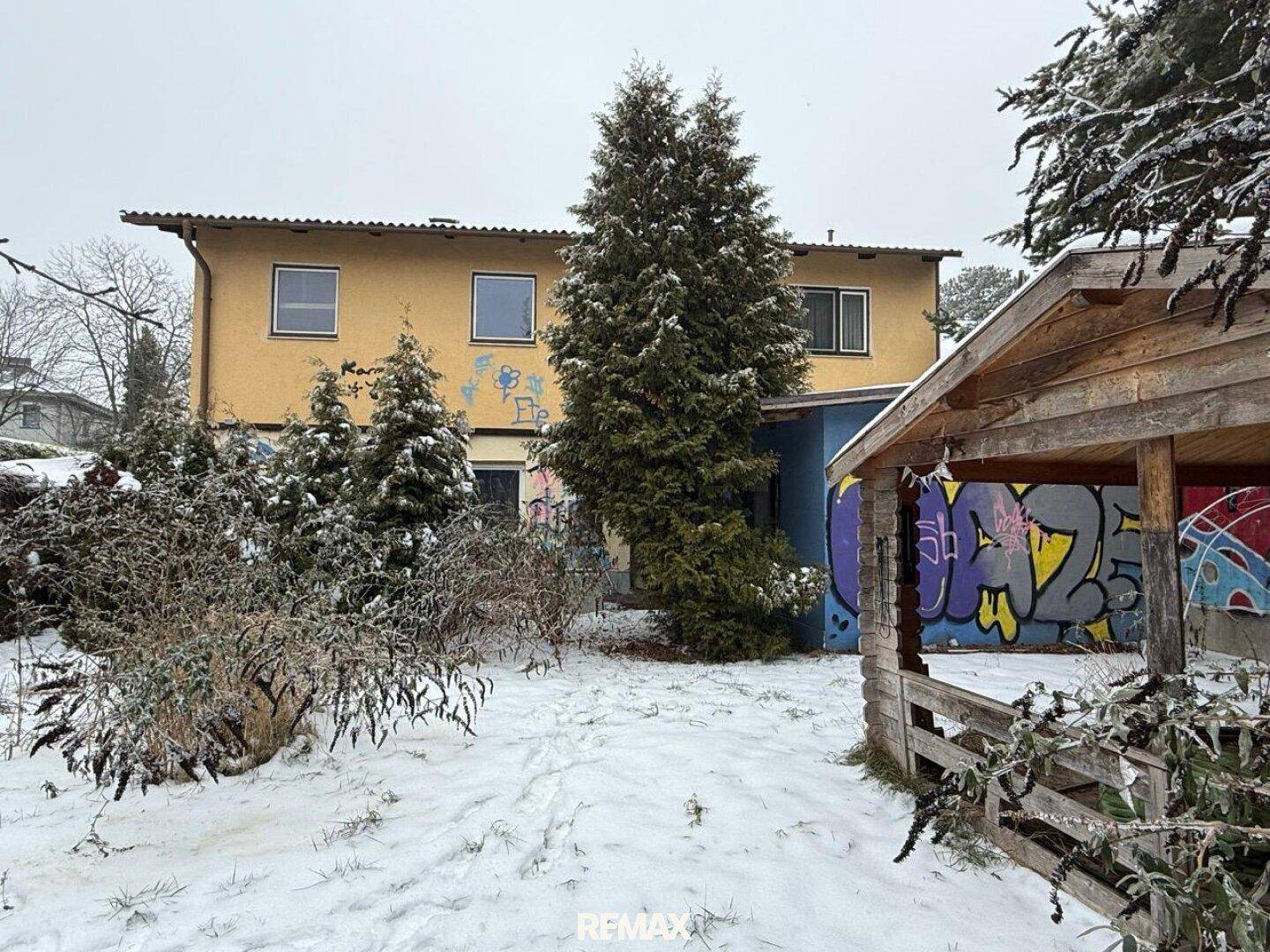 Winterlicher Garten mit verschneiten Bäumen, einem Gartenhaus und dem Haus im Hintergrund.