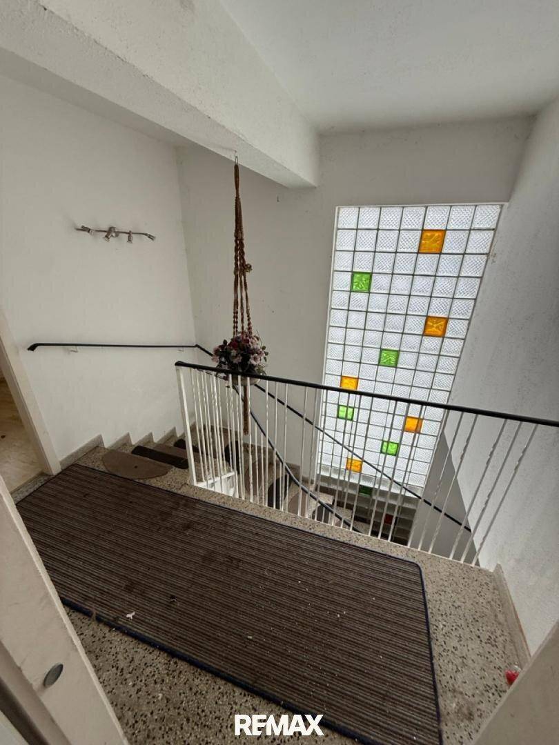 Treppenhaus mit Terrazzoboden, Geländer und einem farbigen Glasbausteinfenster.