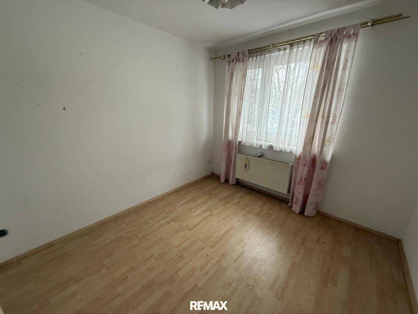 Kleines Schlafzimmer mit Laminatboden, Vorhängen und einem Fenster.