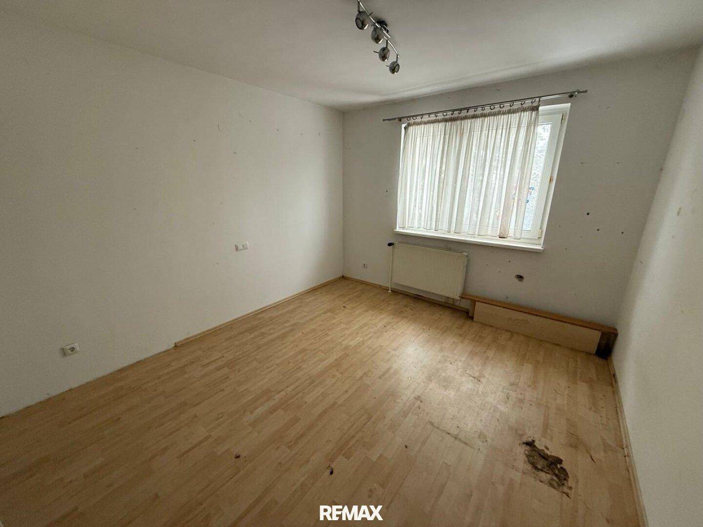 Schlafzimmer mit hellem Laminatboden, einem Fenster und einem Heizkörper.
