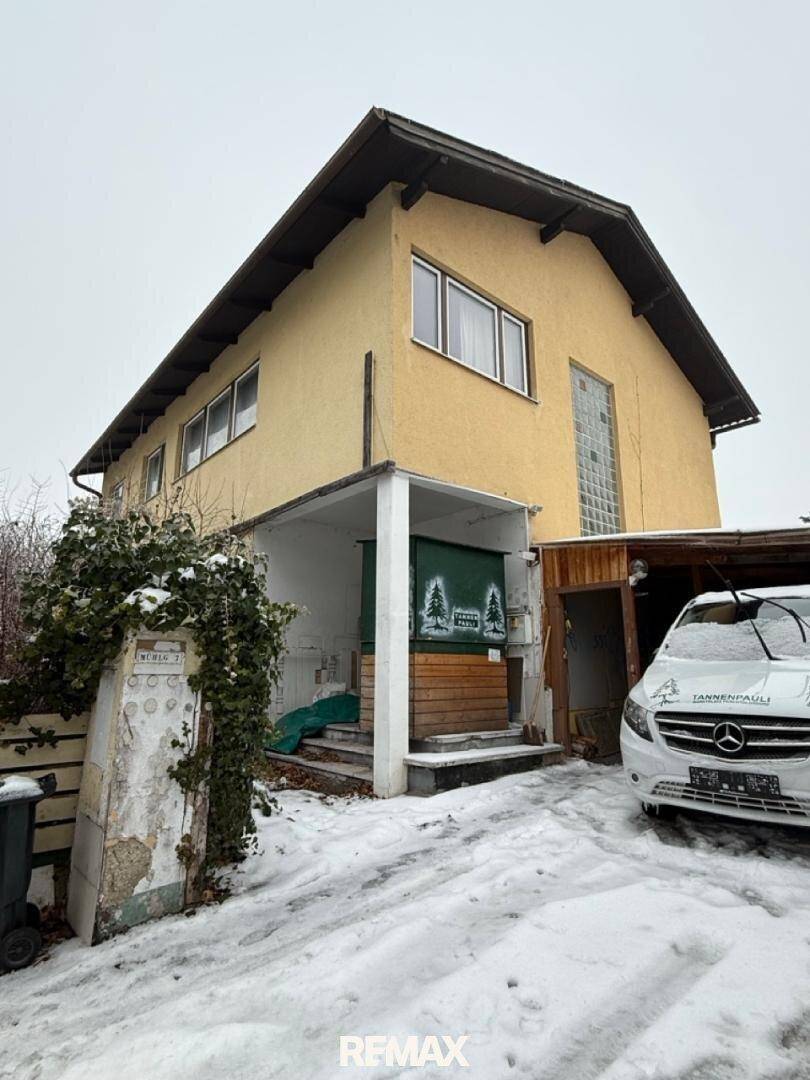Gelbe Hausfassade im Winter mit verschneiter Einfahrt und einem geparkten Auto.