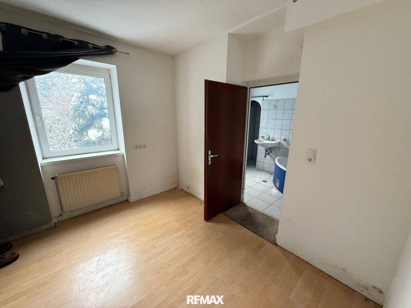 Schlafzimmer mit Laminatboden und Zugang zu einem gefliesten Badezimmer.