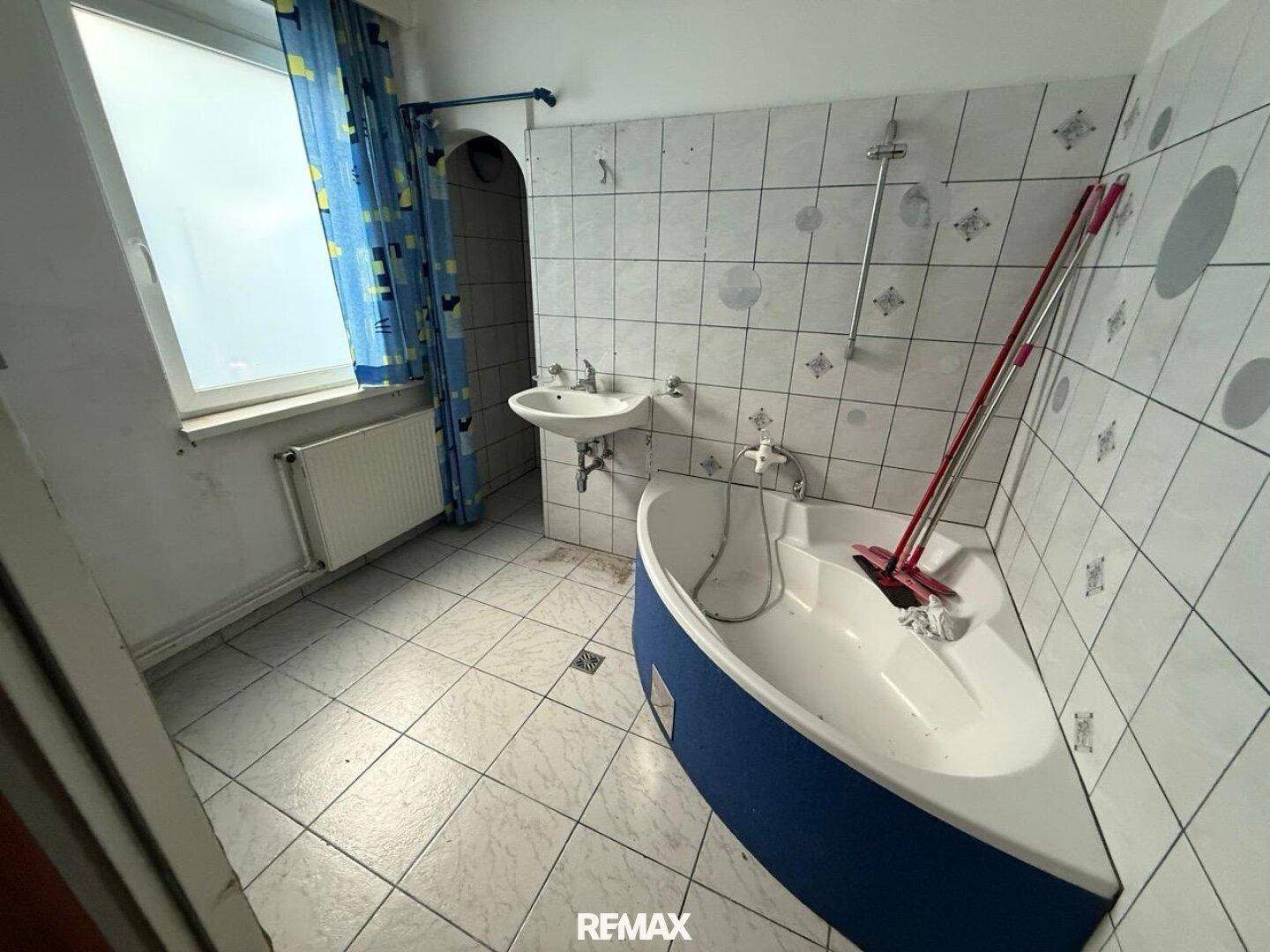 Gefliestes Badezimmer mit Eckbadewanne, Waschbecken und einem Fenster.