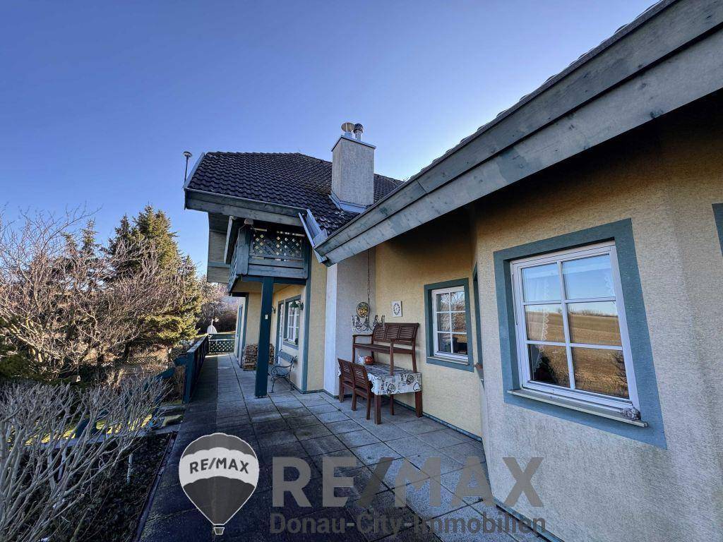 Seitliche Terrasse mit Sitzbank, gepflastertem Boden und Blick auf die umliegende Landschaft.