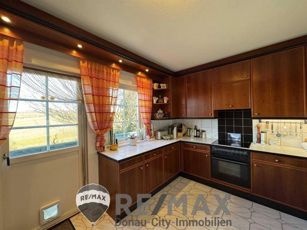 Küche im Landhausstil mit Holzschränken, Fliesenboden und Fenster mit Blick ins Grüne.