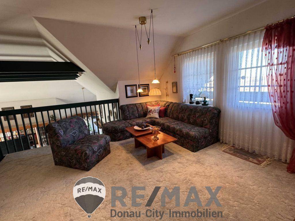 Obergeschoss-Wohnbereich mit Teppichboden, bequemer Sitzecke und großen Fenstern.