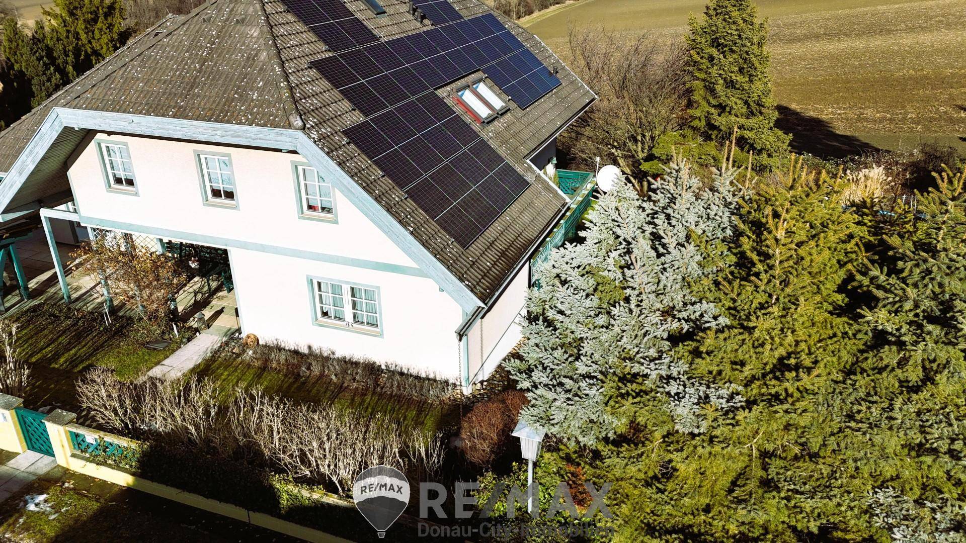 Nahaufnahme des Hauses von oben mit Solaranlage auf dem Dach und umliegenden Bäumen.