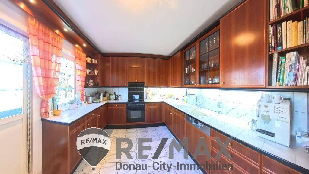 Geräumige Holzküche mit vielen Schränken, Fliesenboden und Arbeitsplatten aus hellem Material.