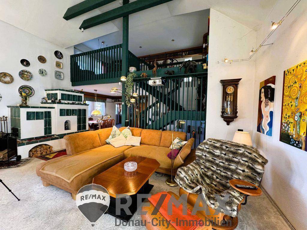 Gemütliches Wohnzimmer mit Kachelofen, großer Couch und Blick auf die Galerie mit Holzgeländer.