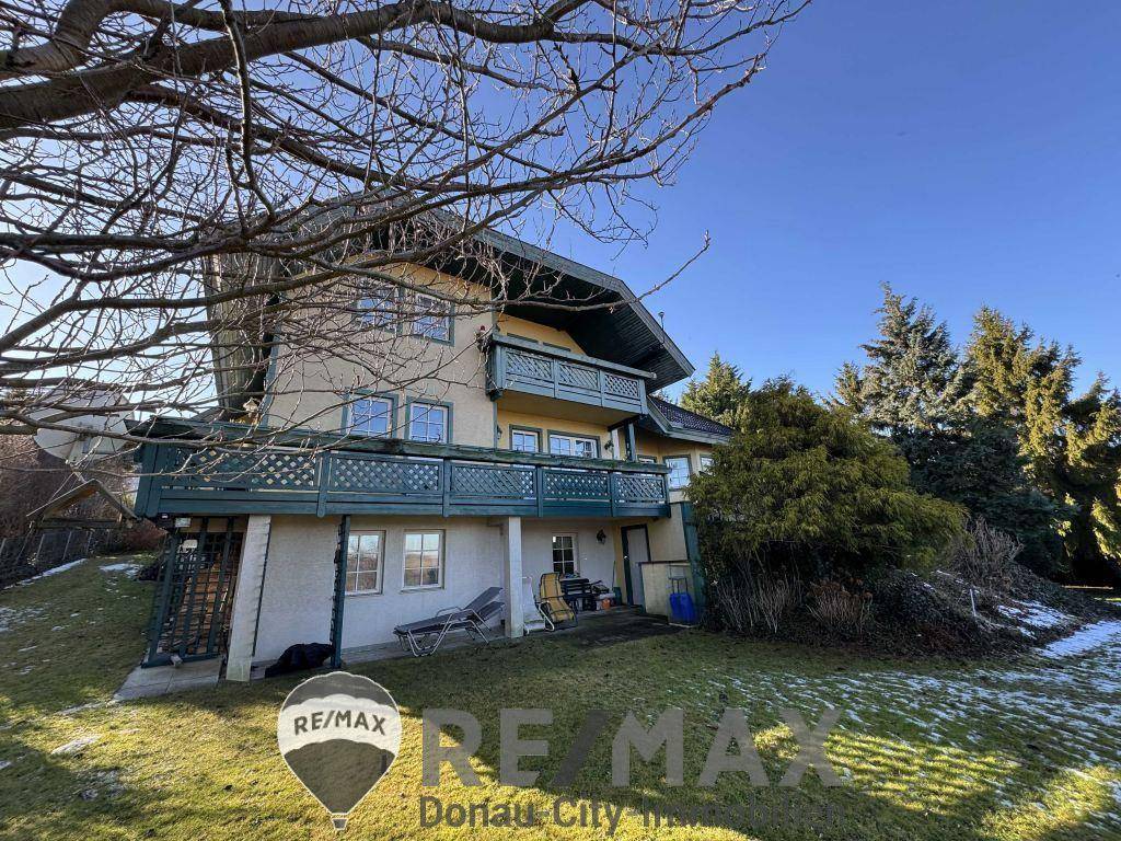 Rückseite des Hauses mit Garten, Rasenfläche und Balkonen im Obergeschoss.