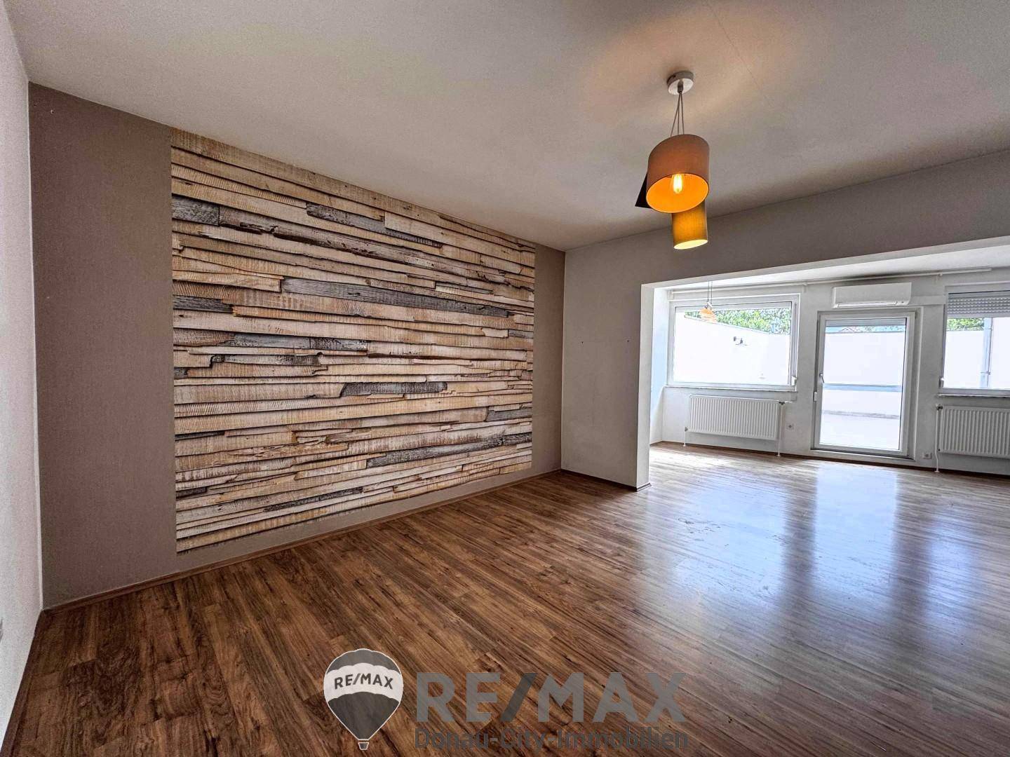 Geräumiges Wohnzimmer mit dekorativer Holzwand und großen Fenstern für viel Licht.