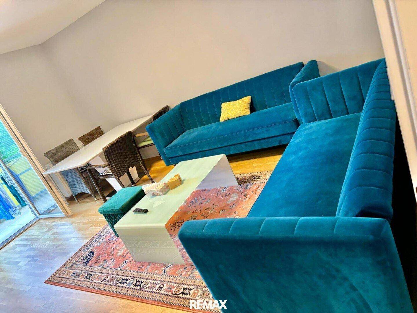 Geräumiger Wohn- und Essbereich mit auffälligen blauen Sofas und Holzboden.