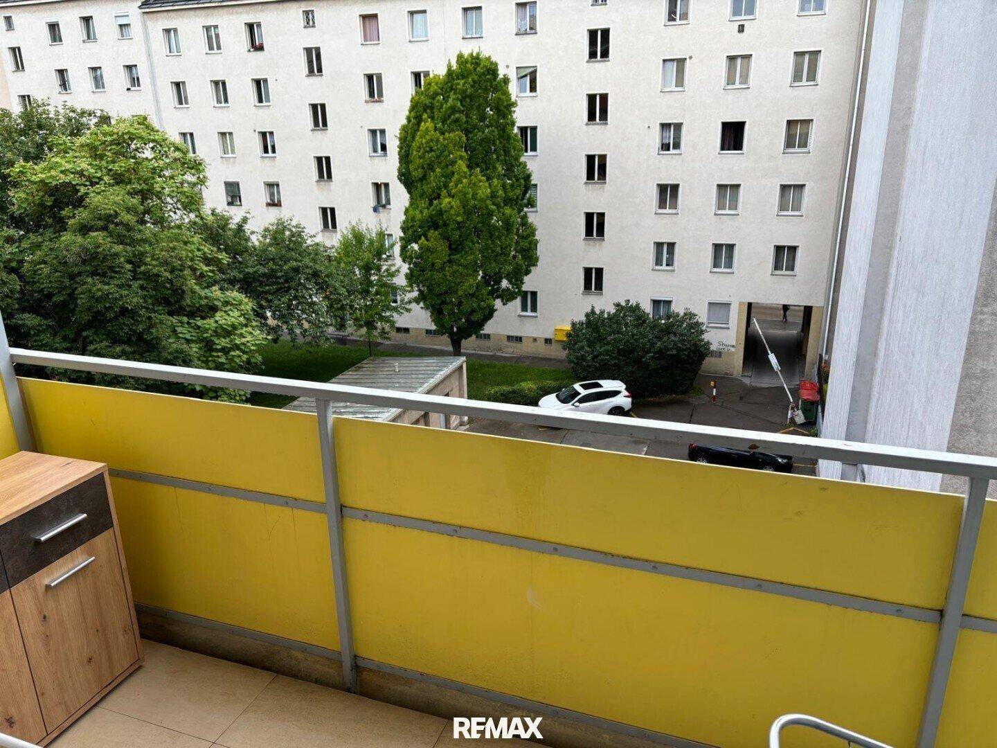 Balkon mit Blick auf einen grünen Innenhof und die umliegenden Wohngebäude.