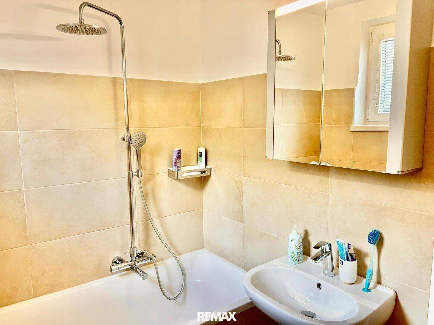 Funktionales Badezimmer mit Badewanne, Duschfunktion, Waschbecken und Spiegelschrank.