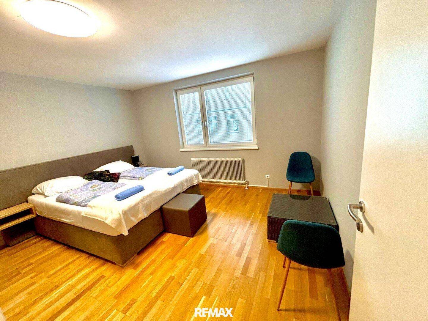 Helles Schlafzimmer mit Doppelbett, Holzboden und Fenster mit Blick nach draußen.