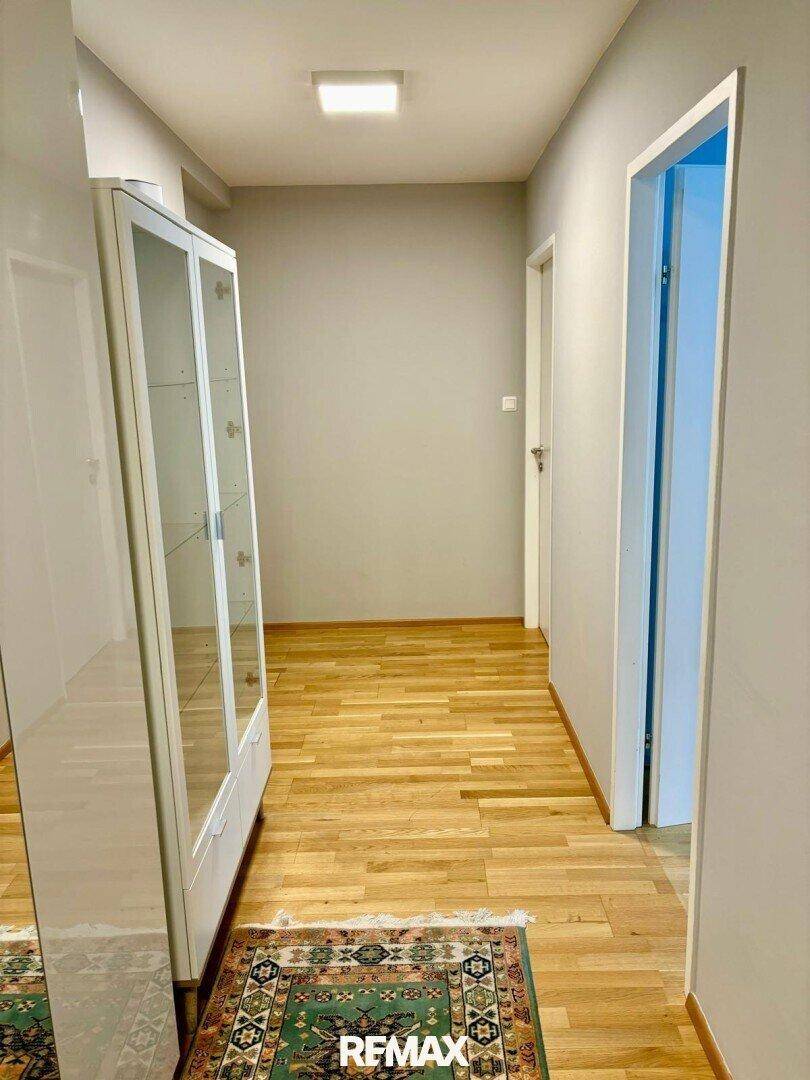 Heller Flur mit Holzboden und einem weißen Vitrinenschrank.