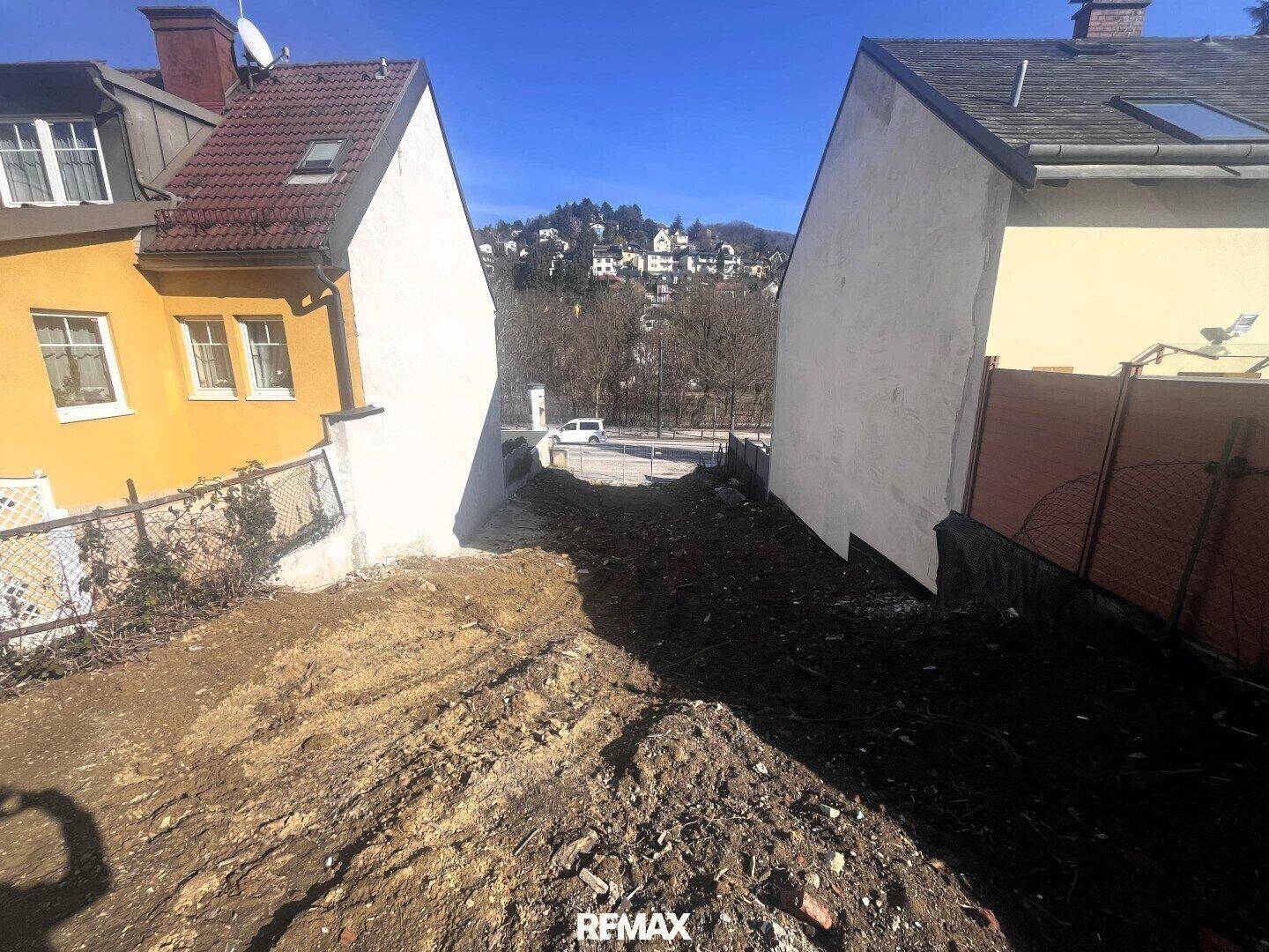 Schmales Grundstück zwischen zwei Häusern mit Blick auf die gegenüberliegende Hügellandschaft.