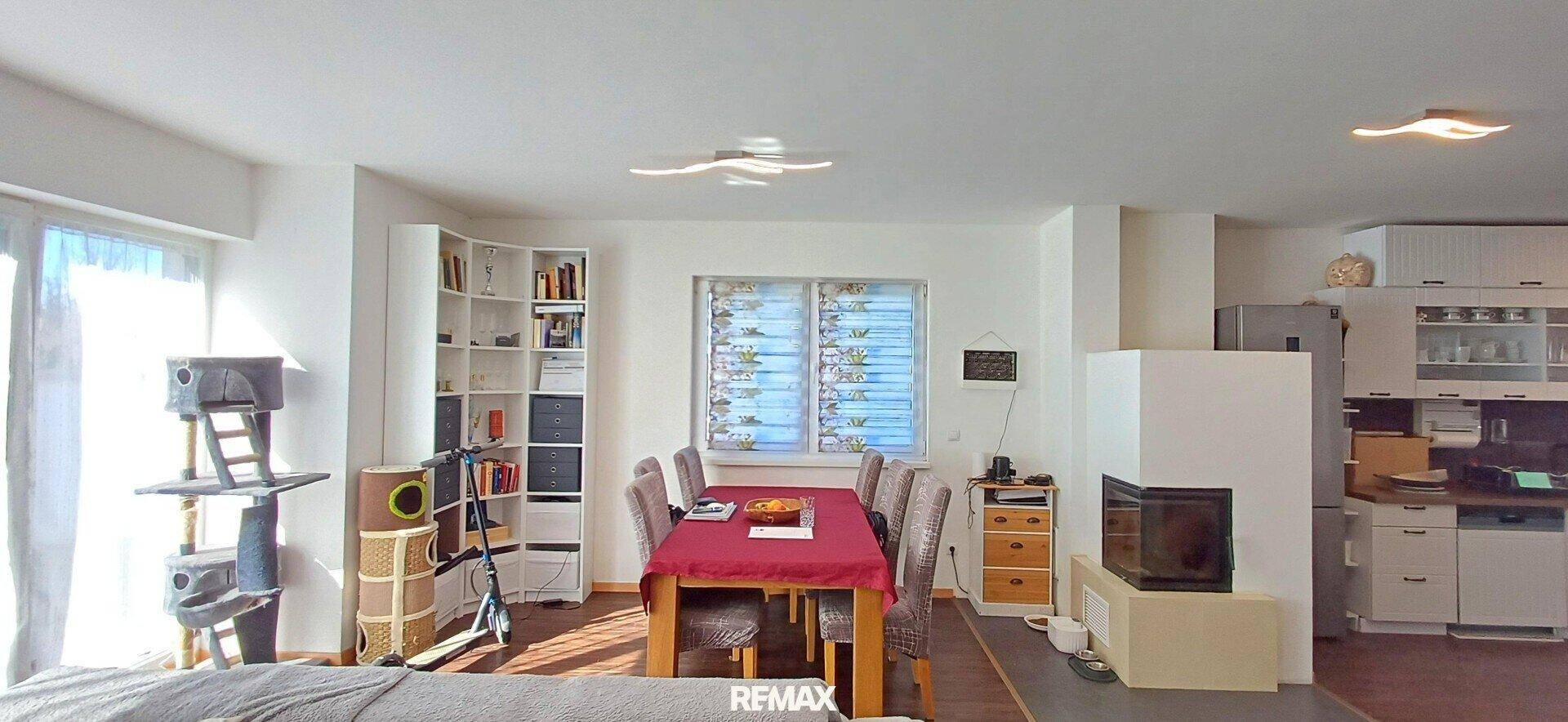 Geräumiger Wohn- und Essbereich mit Kamin, Esstisch und Blick in die angrenzende Küche.