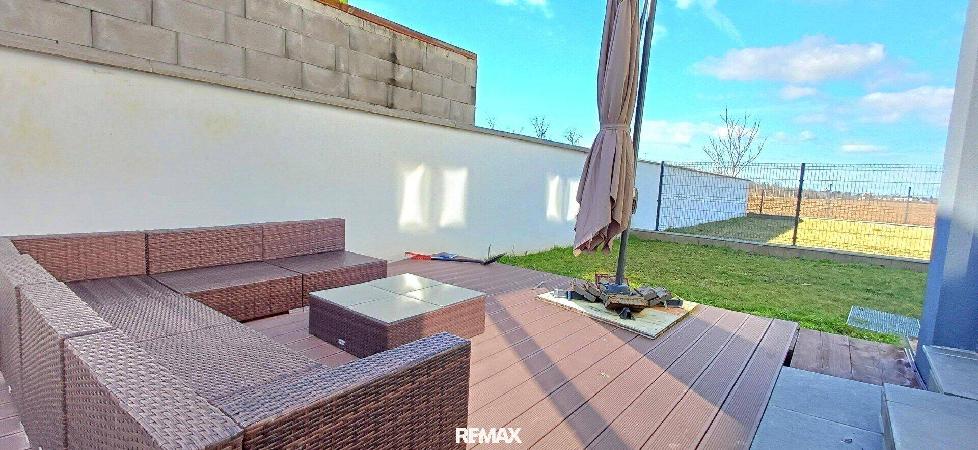 Gemütliche Terrasse mit Rattan-Sitzgruppe, Sonnenschirm und Zugang zum Garten.