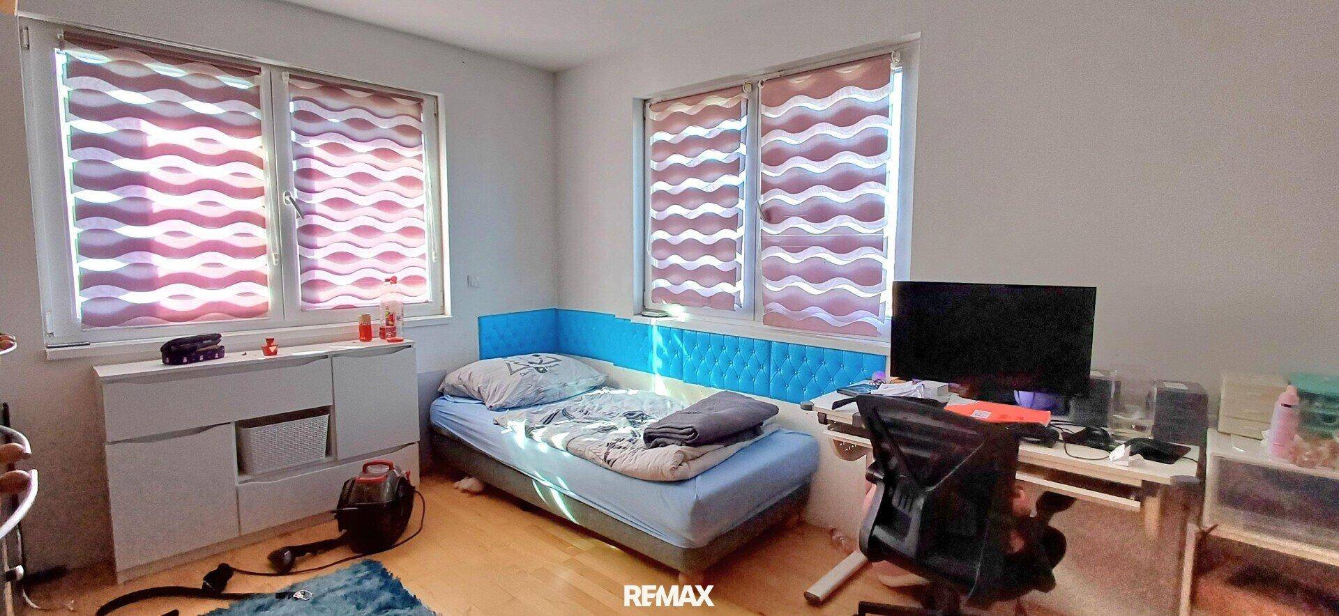 Kinder- oder Gästezimmer mit Einzelbett, Schreibtisch und zwei Fenstern.
