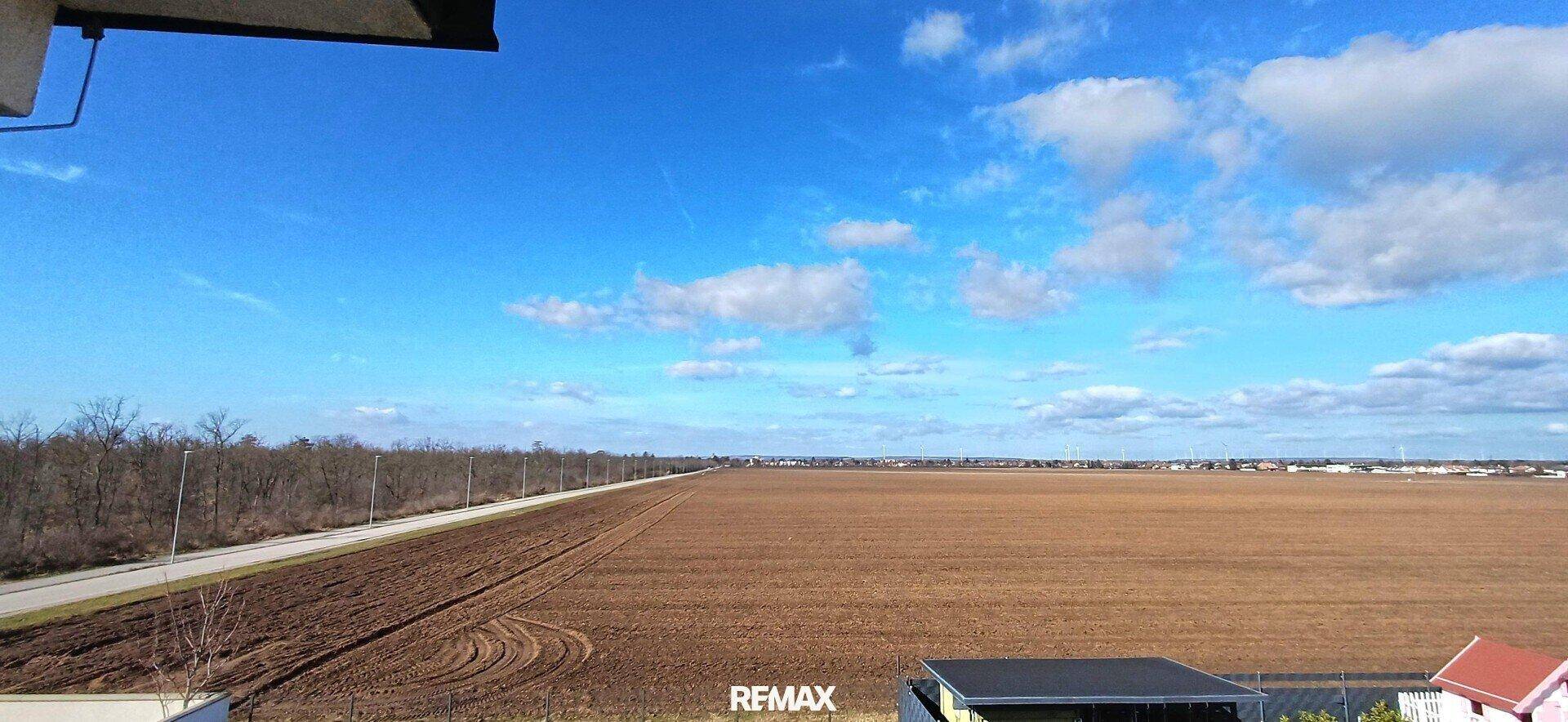 Weitläufiger Blick über Felder und die ländliche Umgebung unter blauem Himmel.